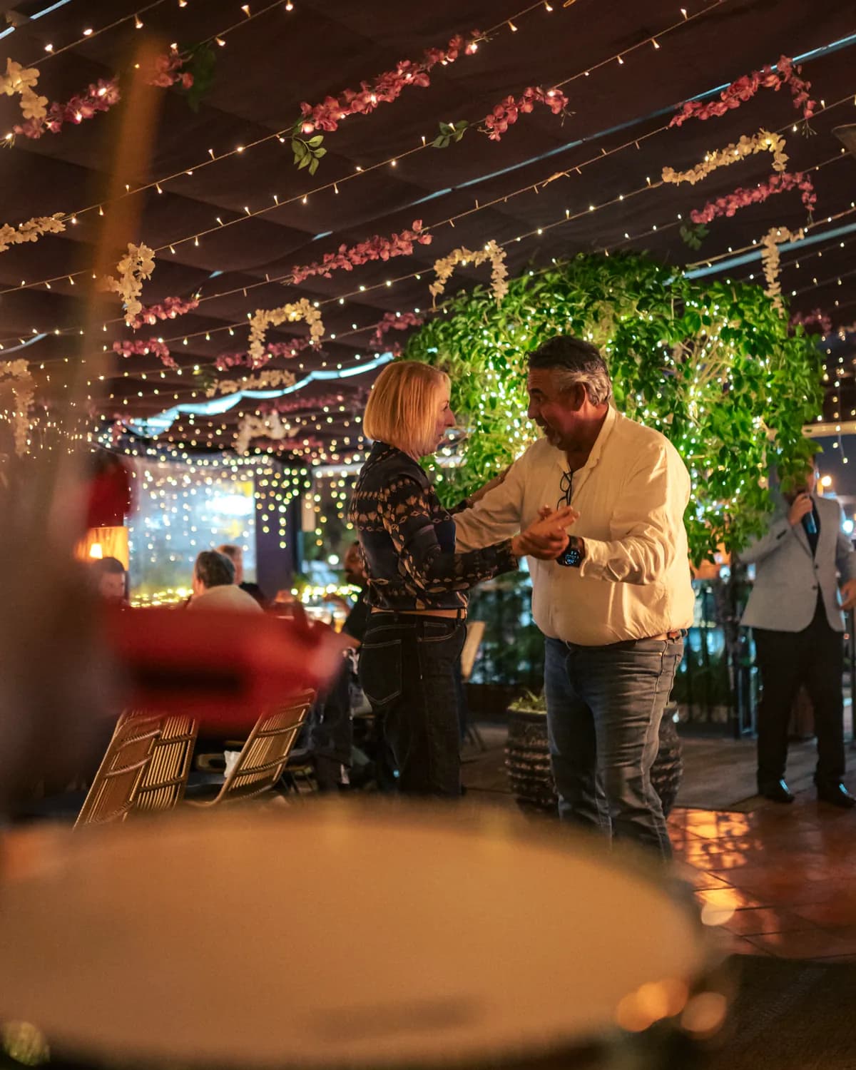 Guests dining while a singer performs and a couple dances under the string lights at Pachamama